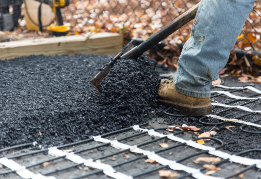 Alt Text: a contractor shoveling asphalt material for a heated driveway