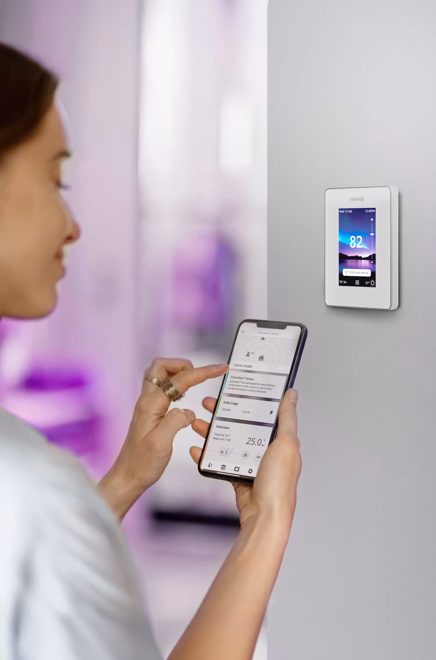 A woman using her phone to control Warmup's 7iE Smart Matter Thermostat