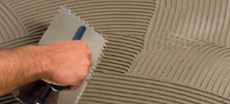 A man spreading thinset on a subfloor to prepare for the installation of underfloor radiant heating
